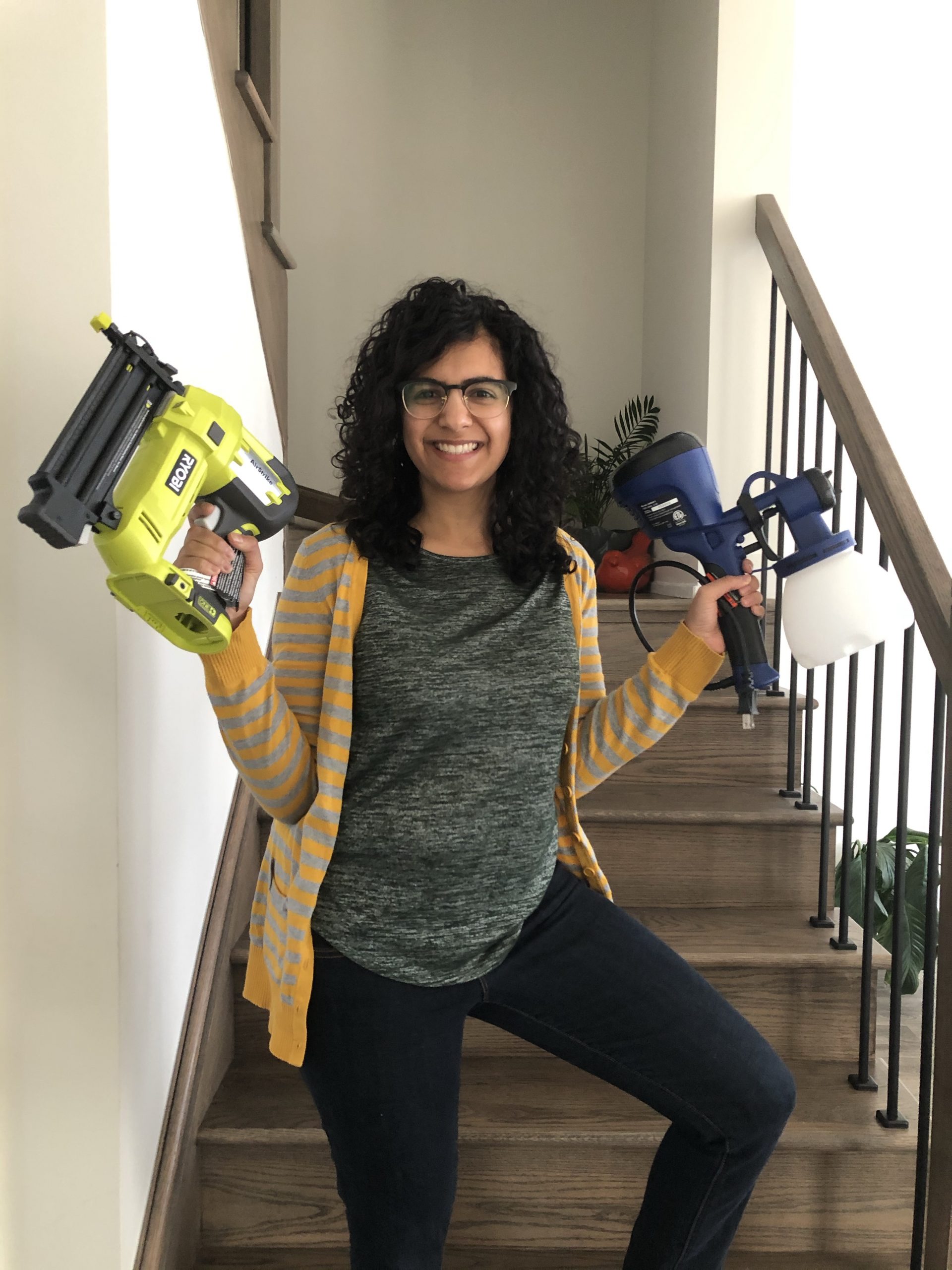 A DIY enthusiast holding a nail gun and paint sprayer, ready to tackle a bathroom accent wall