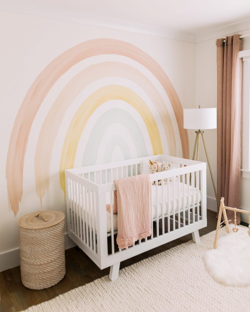 watercolor rainbow arch wall painted mural for baby girls nursery with a white crib