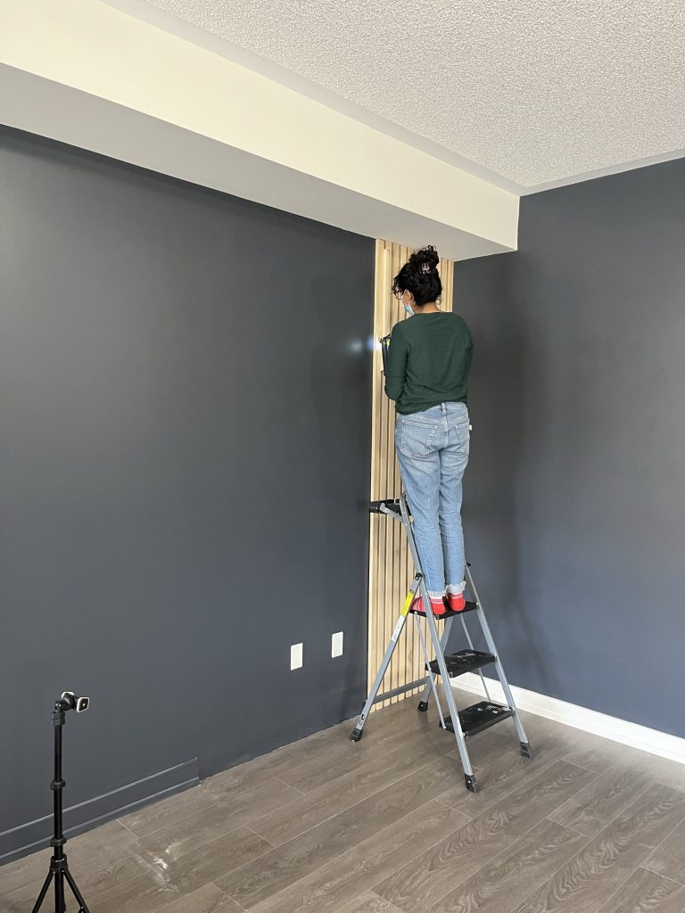 Girl standing on a ladder with a nail gun, nailing in the slats