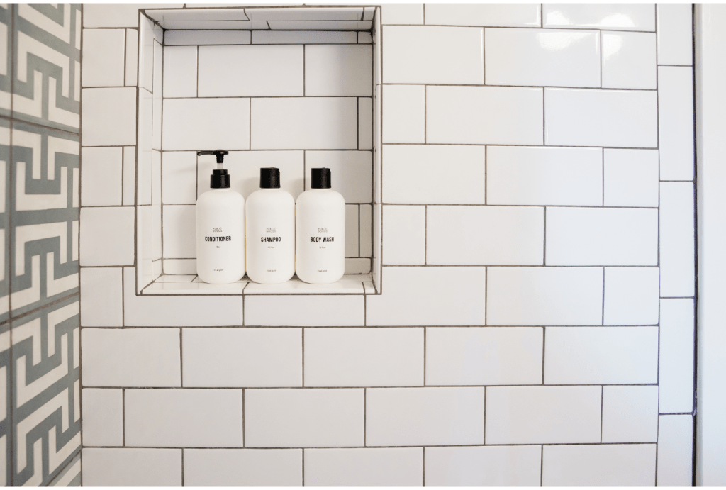 2024 design trend is to minimize clutter with built in recessed shower nook with beautiful shampoo bottles.