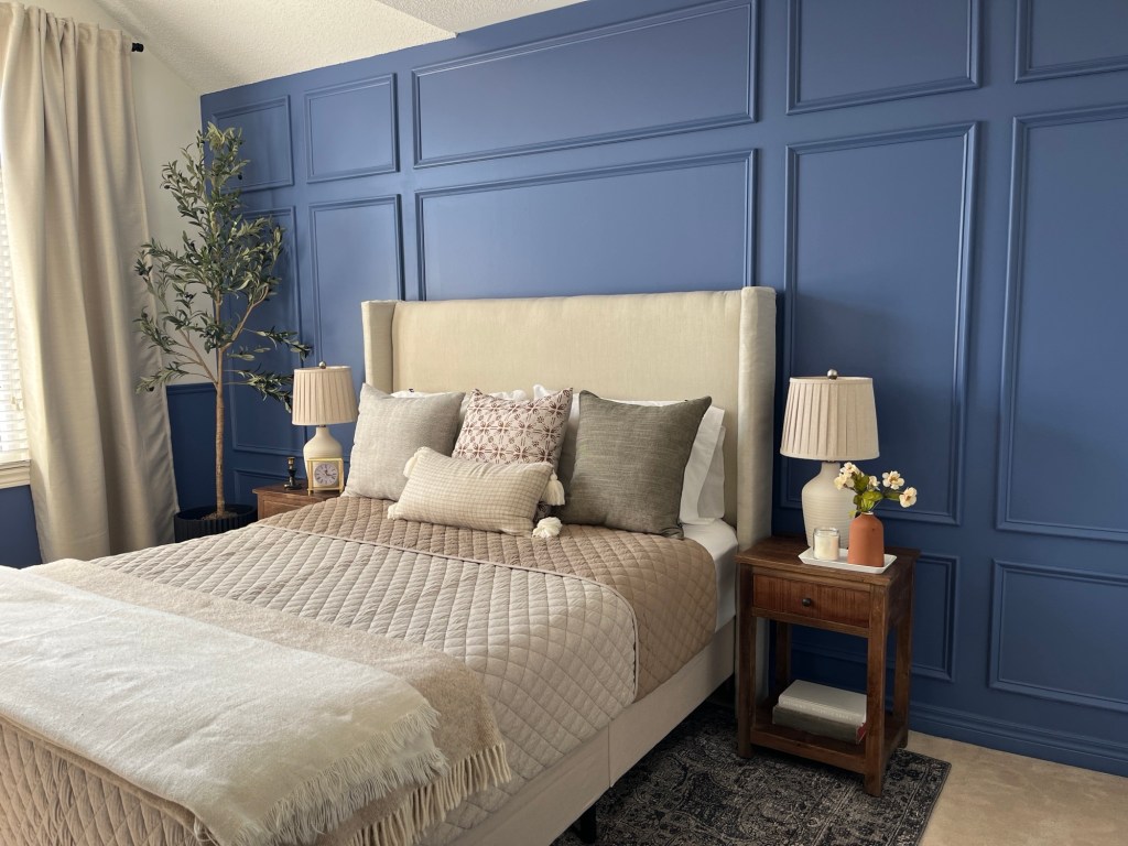 a bedroom that looks fresh with a cream colored upholestered headboard and linens, and a blue accent wall